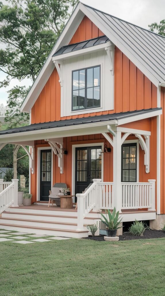 Small gabled farmhouse exterior clad in vibrant orange-red vertical siding, contrasted by white porch railings and posts, a dark metal roof, and black-framed doors.