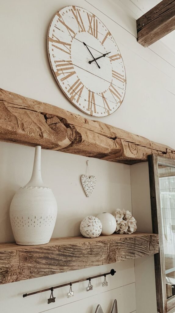 Close-up view of a distressed white Roman numeral clock positioned above a very thick, rough-hewn wooden beam mantel, with a small black hook rail visible underneath.