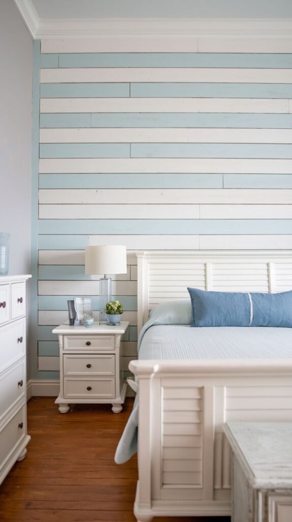 A bright, coastal bedroom featuring a headboard wall of horizontal shiplap planks painted in alternating stripes of white and light blue.