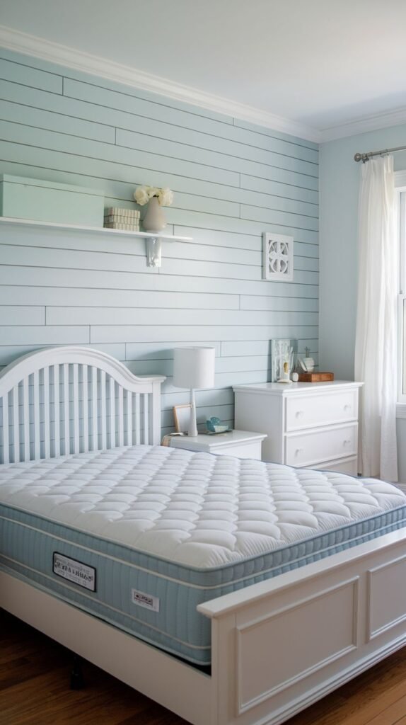 A bright, coastal-themed bedroom featuring a white frame bed with a quilted mattress, set against a soft pastel blue horizontal shiplap accent wall.