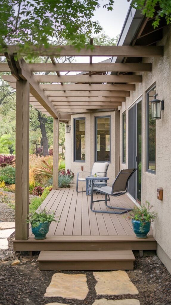 Long elevated wood deck with an open wooden pergola structure. Furnished with dark metal cushioned chairs overlooking a colorful landscaped area.
