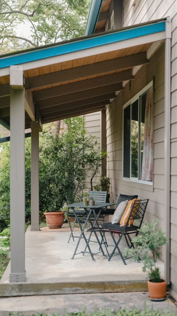 Covered concrete patio with a shed roof structure featuring exposed wood underside and supported by a painted post. Furnished with black metal outdoor chairs and a small table.