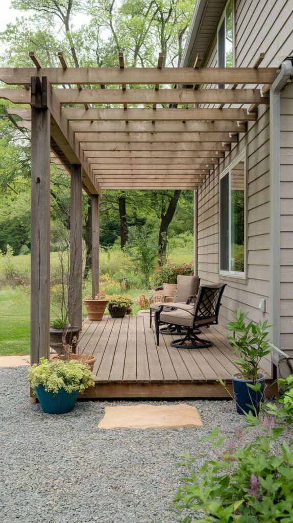 Elevated wood deck covered by an open wooden pergola structure. Furnished with cushioned outdoor chairs, bordered by gravel landscaping.