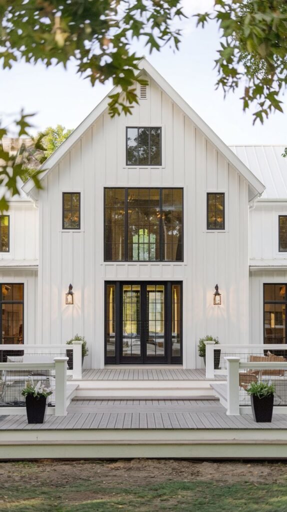 Close-up, symmetrical view of a central white farmhouse entry. The entry features a light gray deck and white railing system framing the black French doors and the dramatic stacked black-framed windows above.