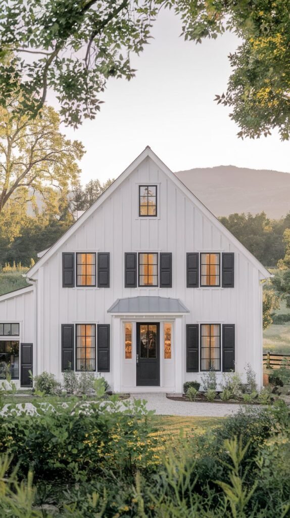 Classic white two-story farmhouse framed by trees. The facade is adorned with contrasting black shutters on black-framed windows, focusing on the dark entry door sheltered by a small portico.