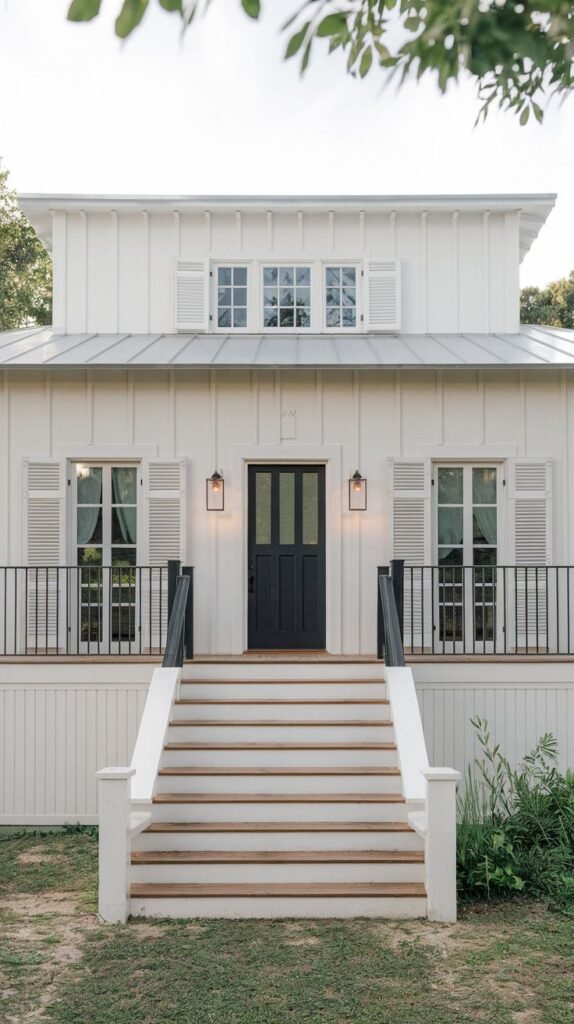Close-up of an elevated white farmhouse porch and entrance. A wide staircase with wood treads leads up to the porch, which features black metal railings and white windows accented with white shutters.